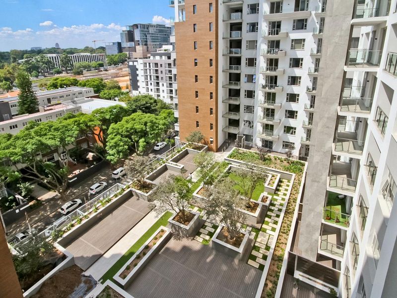 An elevated aerial view of a modern high-rise penthouse complex featuring a landscaped terrace with raised garden beds, decking, and paved walkways.