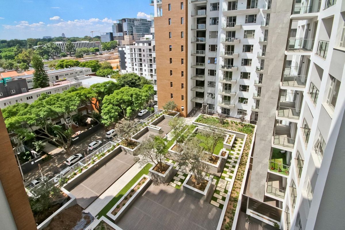An elevated aerial view of a modern high-rise penthouse complex featuring a landscaped terrace with raised garden beds, decking, and paved walkways.
