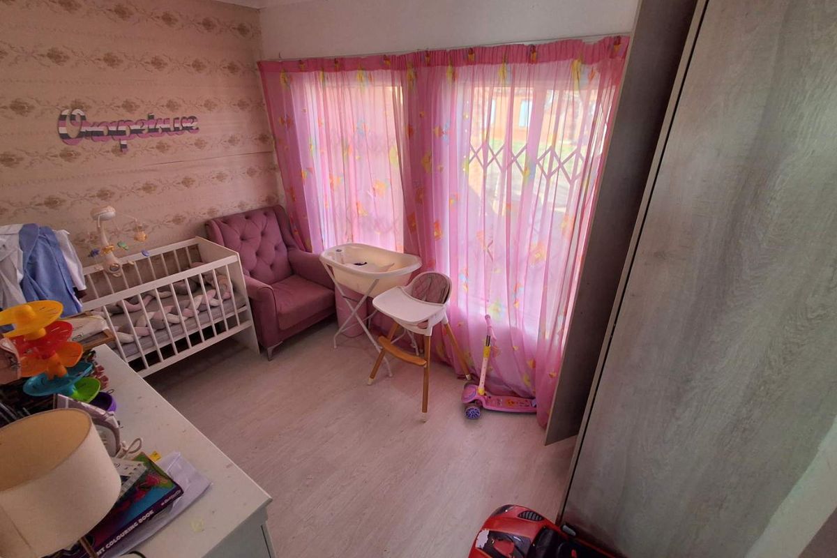 A bedroom featuring light wood-look flooring, built-in cabinetry, and a large window fitted with a security gate.