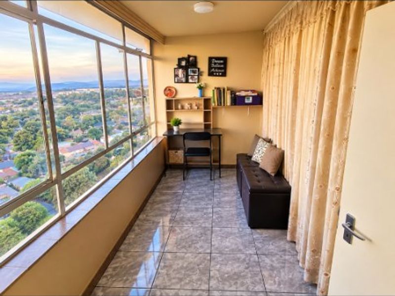 Enclosed balcony featuring large glass windows with panoramic views and tiled flooring, suitable for use as a sunroom or home office space.