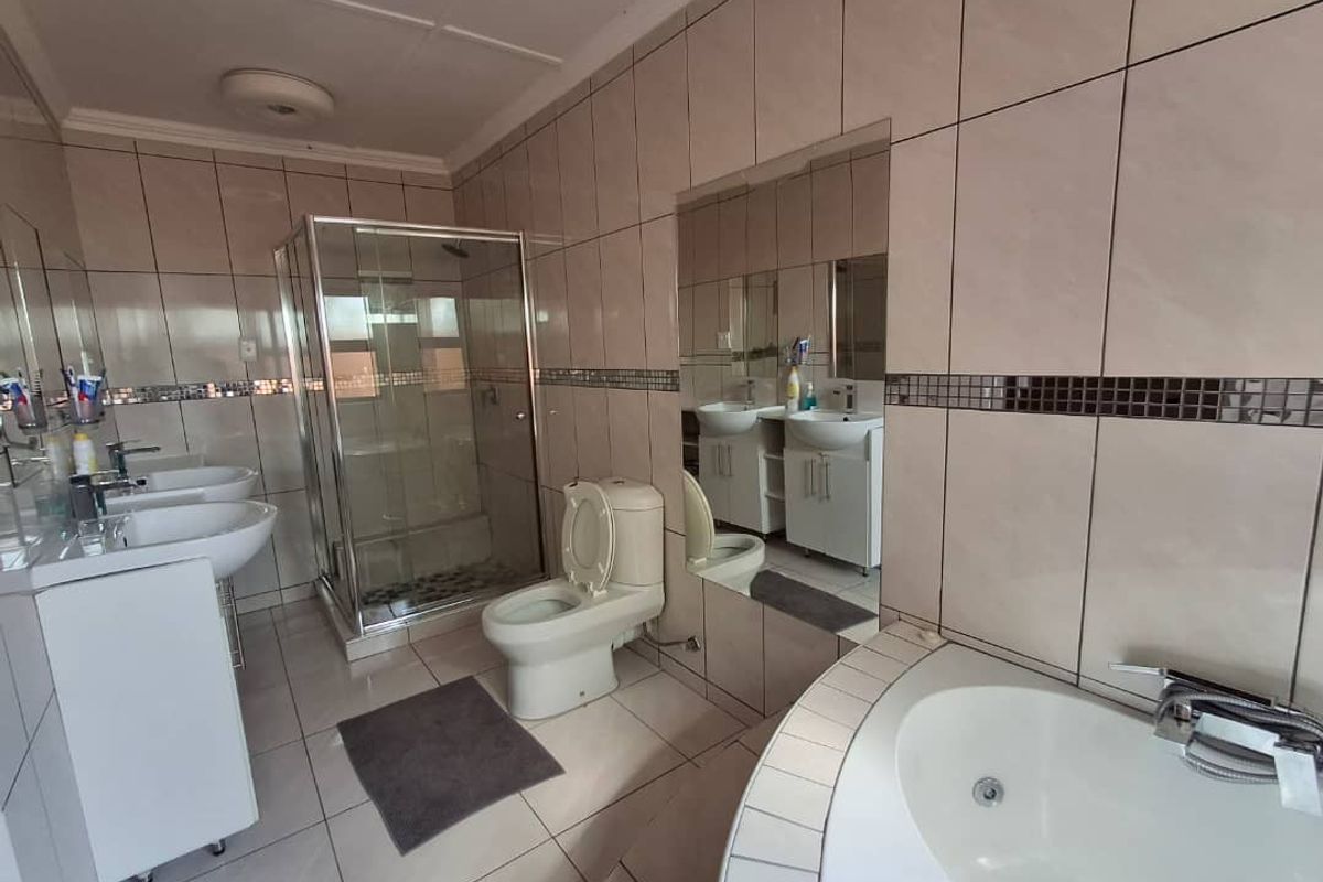 A spacious bathroom featuring a corner bathtub, a glass-enclosed shower, and double vanity basins with integrated storage cabinets.