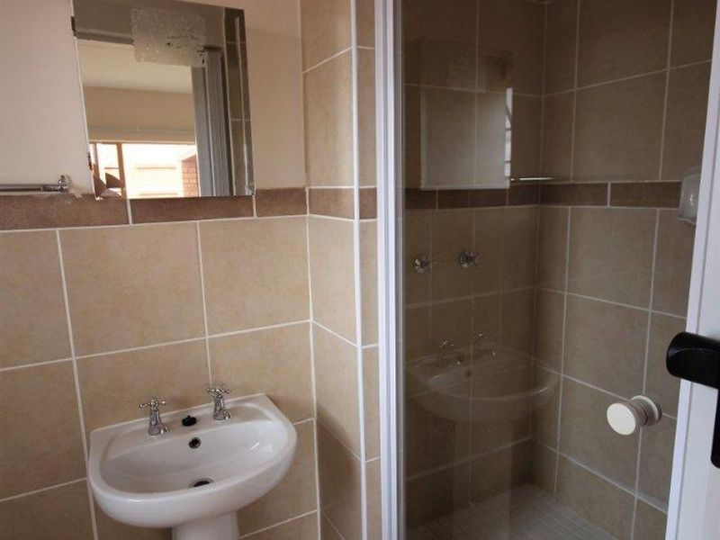 A functional bathroom featuring a pedestal washbasin, a tiled shower enclosure, and neutral wall tiling throughout.