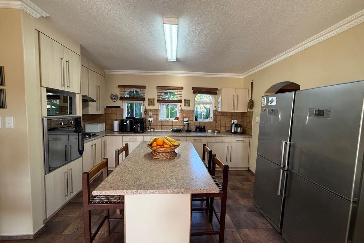 A functional kitchen featuring light-toned cabinetry, a central island with a stone-look countertop, tiled backsplash, and integrated oven and microwave units.