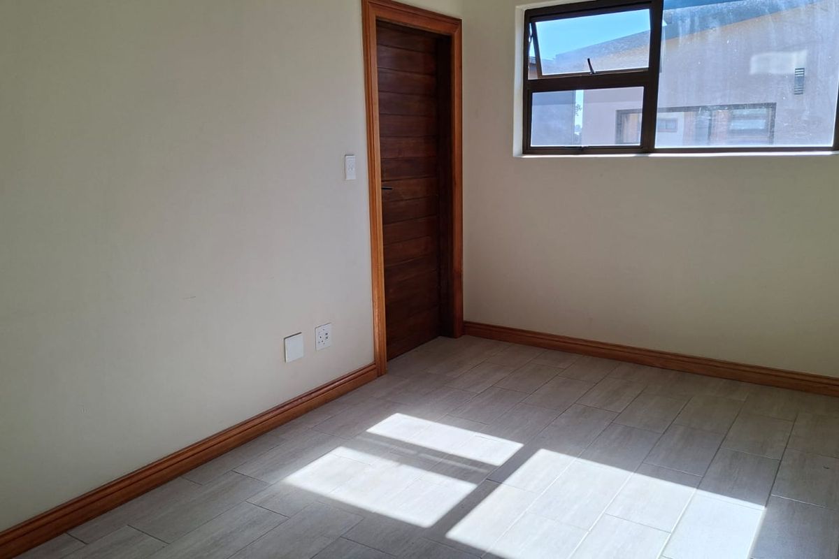 A bright, empty bedroom featuring neutral tiled flooring, wooden door frame, and a top-hung window.