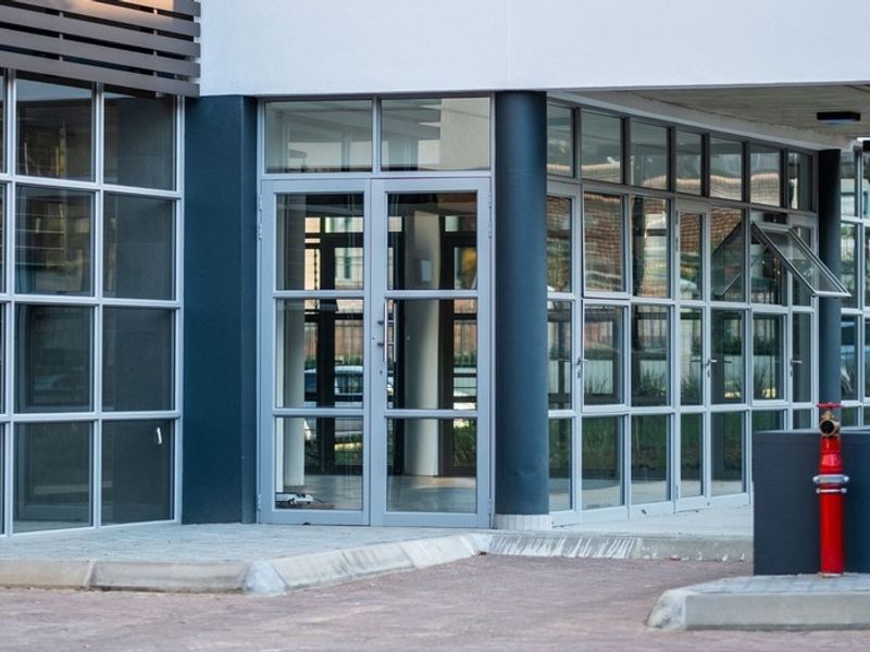 Modern office building exterior featuring extensive glass facade, aluminium framing, and a prominent red fire hydrant at the entrance.