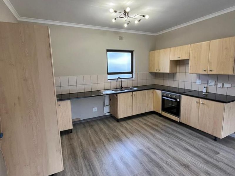 A clean, modern kitchen featuring light wood cabinetry, dark laminate countertops, built-in oven, and durable laminate flooring in an open, well-lit space.