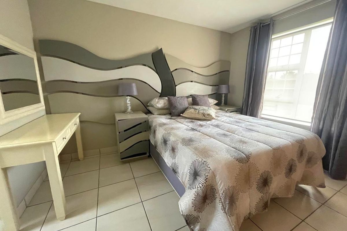 A bedroom featuring tiled flooring, a large window with curtains, and a decorative custom headboard wall feature.