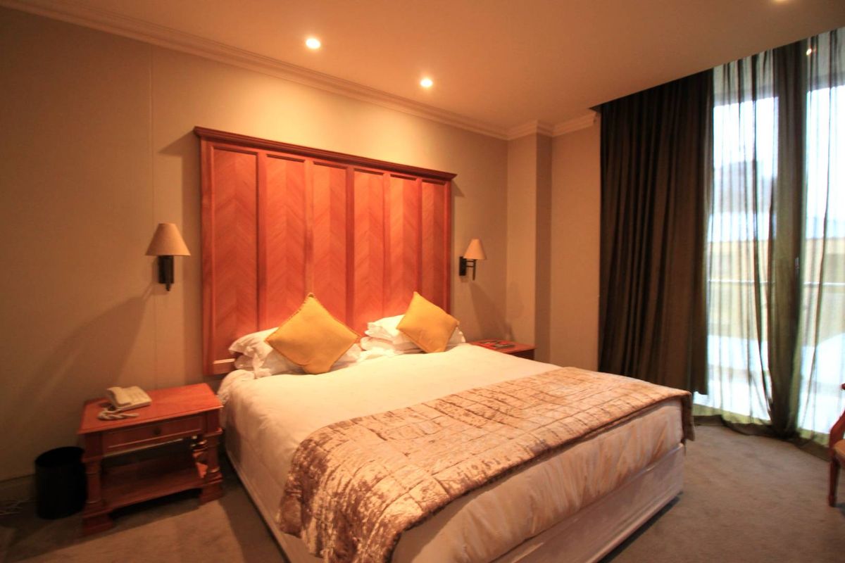 A well-maintained bedroom featuring a custom wooden headboard, recessed ceiling lighting, and floor-to-ceiling curtains leading to a balcony.