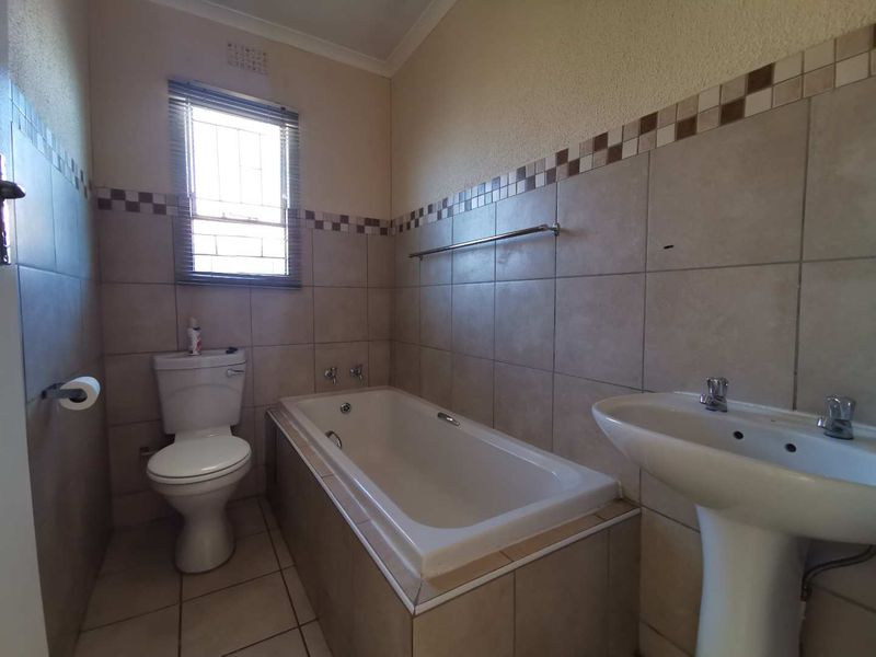 A functional bathroom featuring a bathtub, pedestal basin, and toilet with neutral wall and floor tiling.