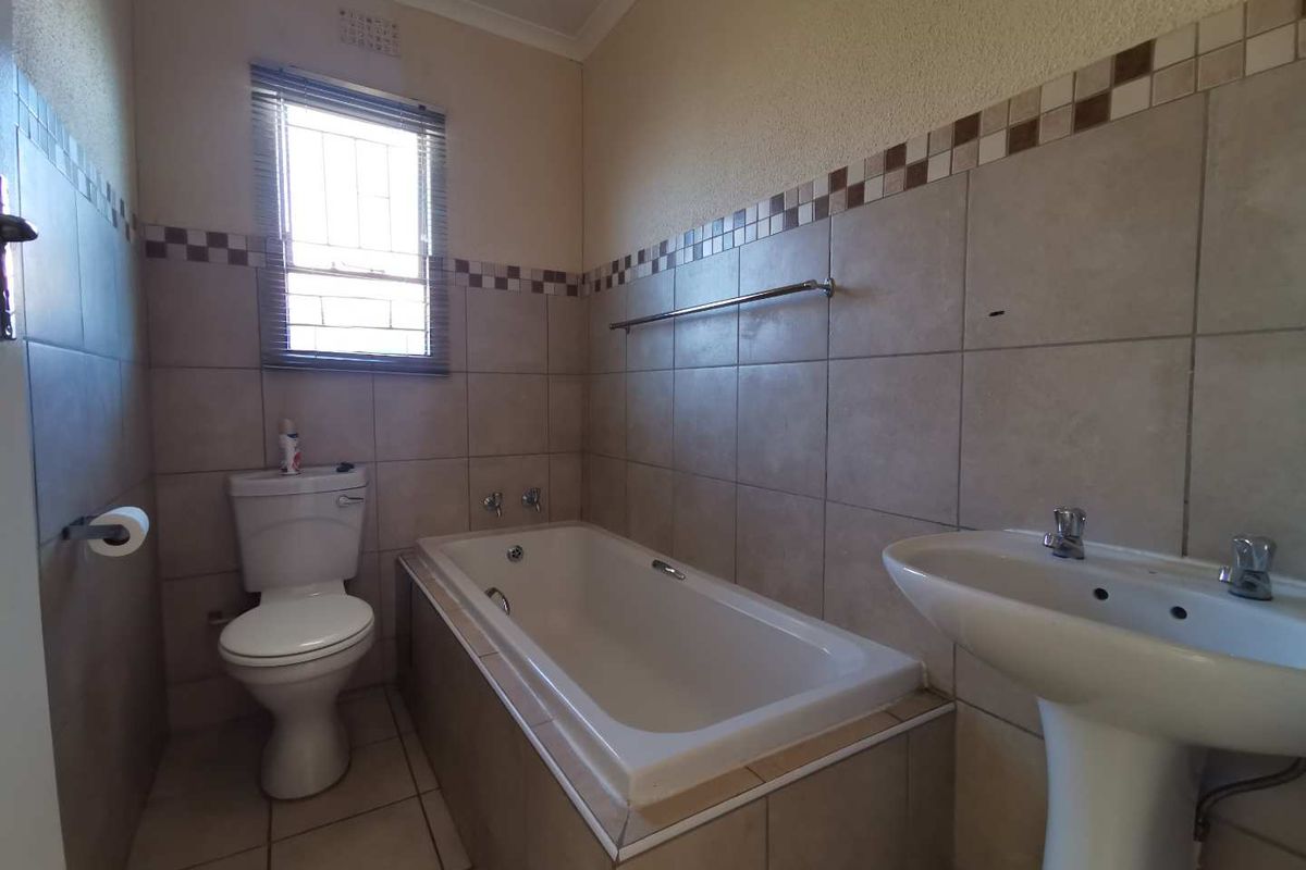A functional bathroom featuring a bathtub, pedestal basin, and toilet with neutral wall and floor tiling.