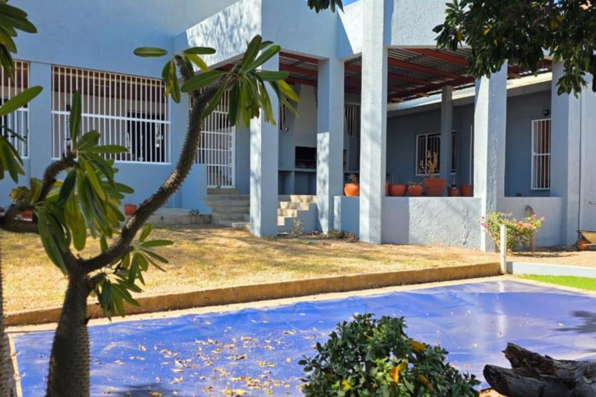 Rear view of the property featuring a covered patio with built-in braai, concrete pillars, and a swimming pool with a safety cover.