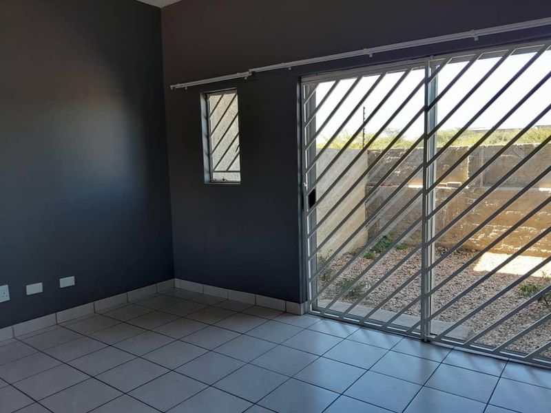 An empty living room featuring tiled flooring, dark grey walls, and a sliding glass door with a security gate leading to an outdoor area.