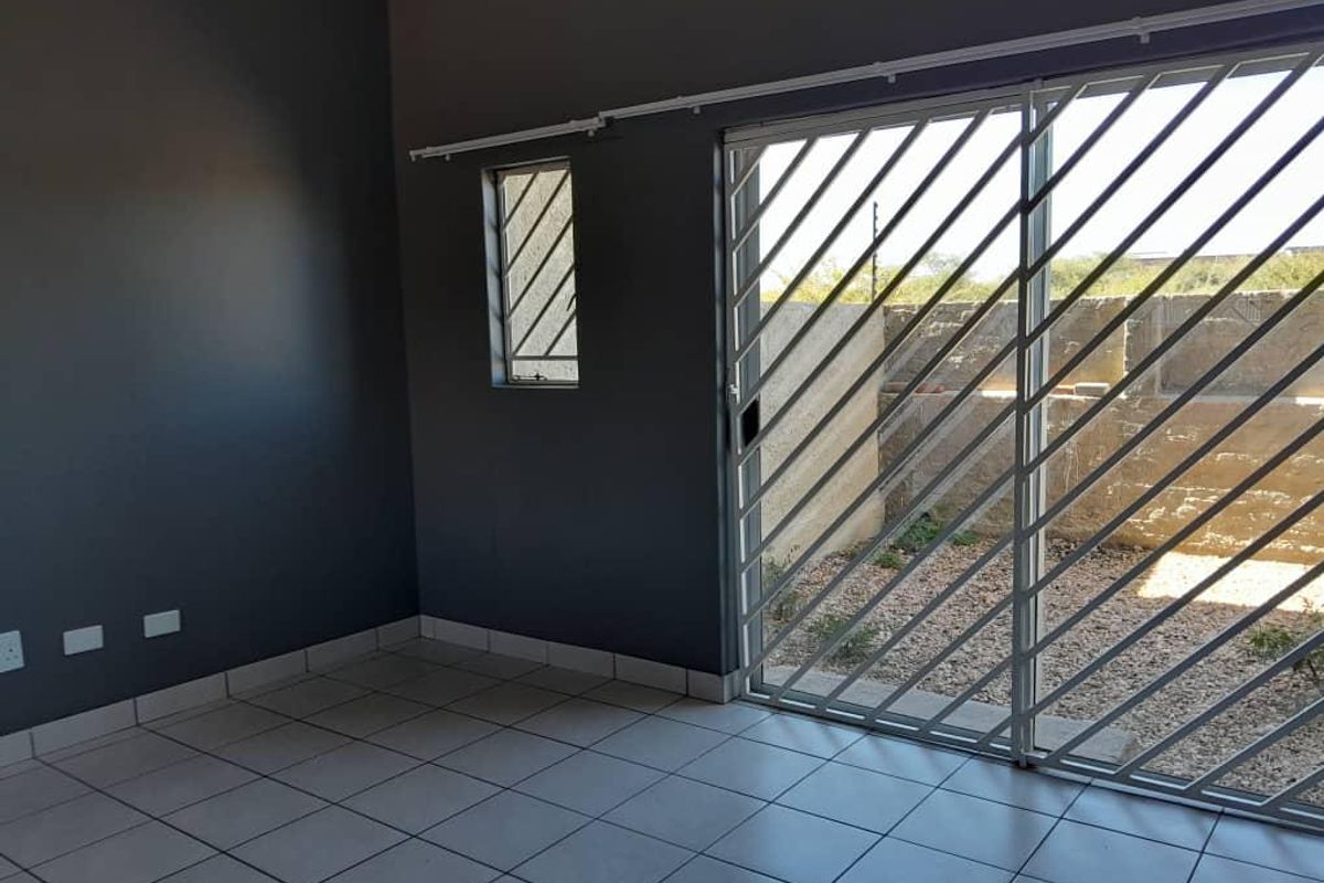 An empty living room featuring tiled flooring, dark grey walls, and a sliding glass door with a security gate leading to an outdoor area.