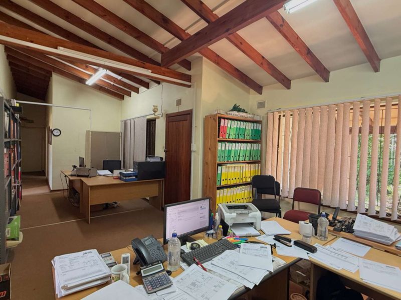 A functional office space featuring exposed timber rafters, vertical blinds, and carpet flooring, providing a practical work environment.