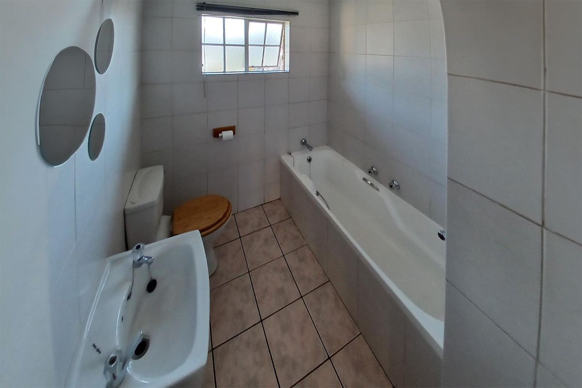 A functional bathroom featuring a bathtub, pedestal basin, and toilet with neutral wall and floor tiling.
