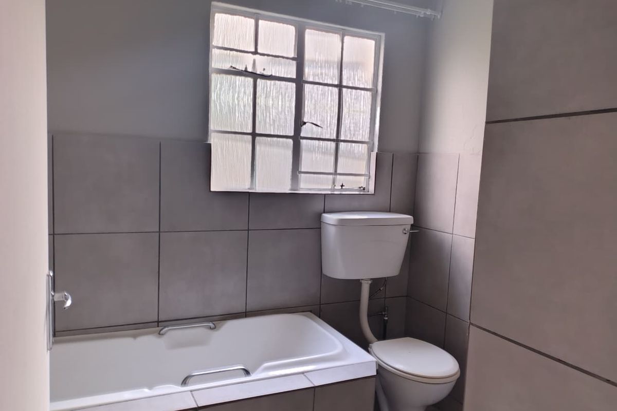 A functional bathroom featuring a bathtub, toilet, and neutral wall tiling, offering a clean canvas for potential modernization.
