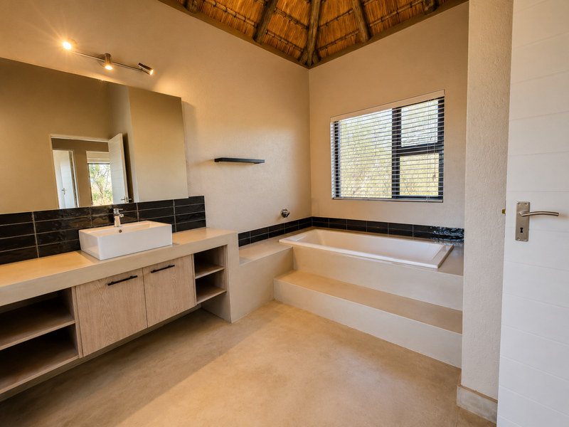 Modern bathroom featuring a built-in vanity with vessel sink, a raised bathtub, and a unique thatched ceiling, offering a clean and contemporary aesthetic.
