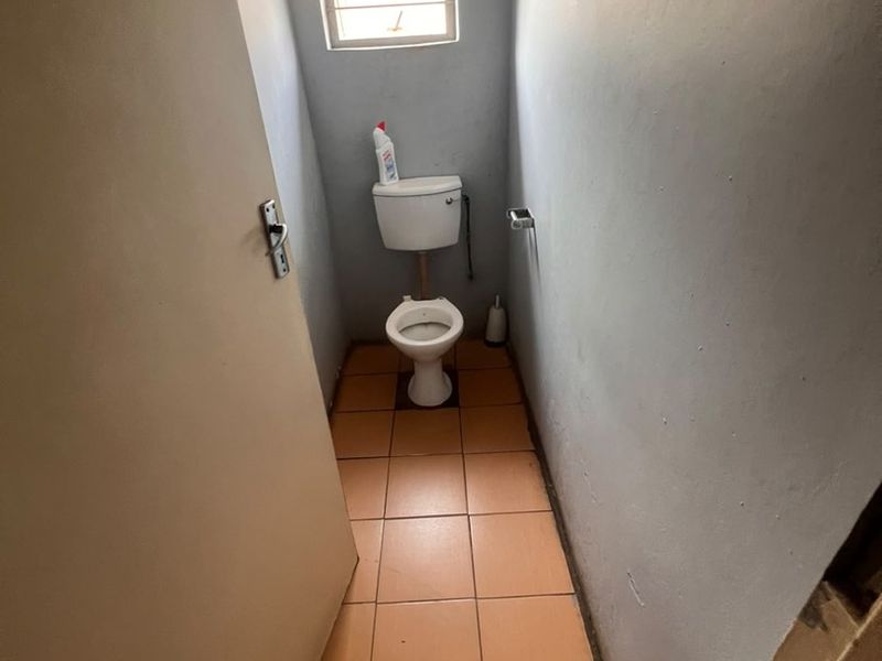 A compact, functional guest toilet featuring ceramic floor tiles and a louvered window, presenting an opportunity for cosmetic modernization.