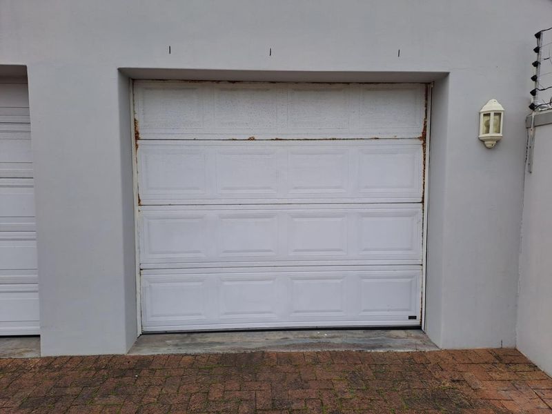 A single garage entrance featuring a white sectional door with visible surface rust, set within a rendered exterior wall.