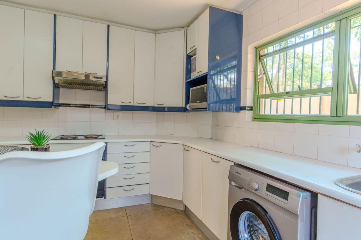 A functional kitchen featuring white and blue cabinetry, tiled splashbacks, a built-in hob, extractor fan, and space for a washing machine.