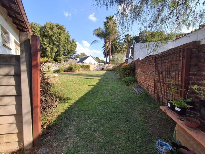 A spacious backyard garden featuring a well-maintained lawn, enclosed by a traditional brick boundary wall and metal gate.