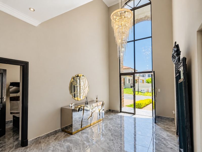 Grand double-volume entrance hall featuring high ceilings, a striking crystal chandelier, large arched window, and polished marble-look floor tiles.