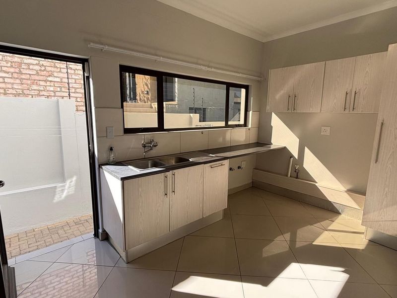 A clean and functional laundry room featuring built-in cabinetry, a double sink, tiled flooring, and direct access to an outdoor area.