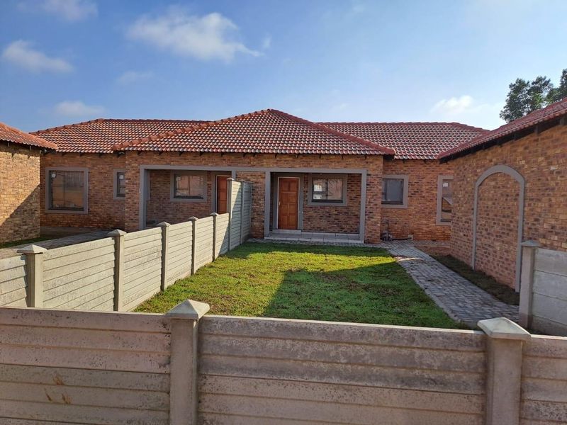 A well-maintained facebrick townhouse featuring a tiled roof, paved walkway, and a private front garden enclosed by precast concrete boundary walls.