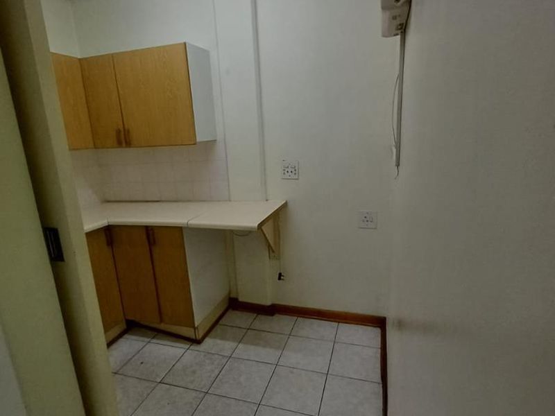 A compact, empty office kitchenette featuring built-in cabinetry, laminate countertops, and tiled flooring, suitable for a small staff break area.