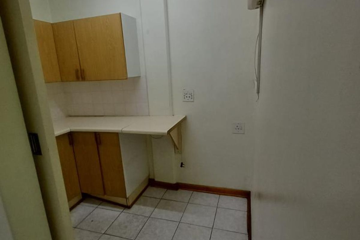 A compact, empty office kitchenette featuring built-in cabinetry, laminate countertops, and tiled flooring, suitable for a small staff break area.