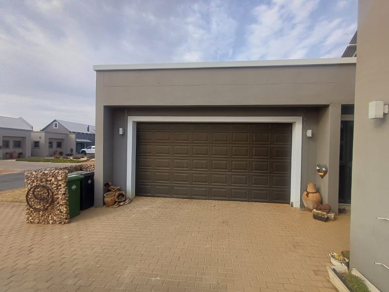 A modern single garage with a dark sectional door and paved driveway, featuring a decorative gabion wall element.