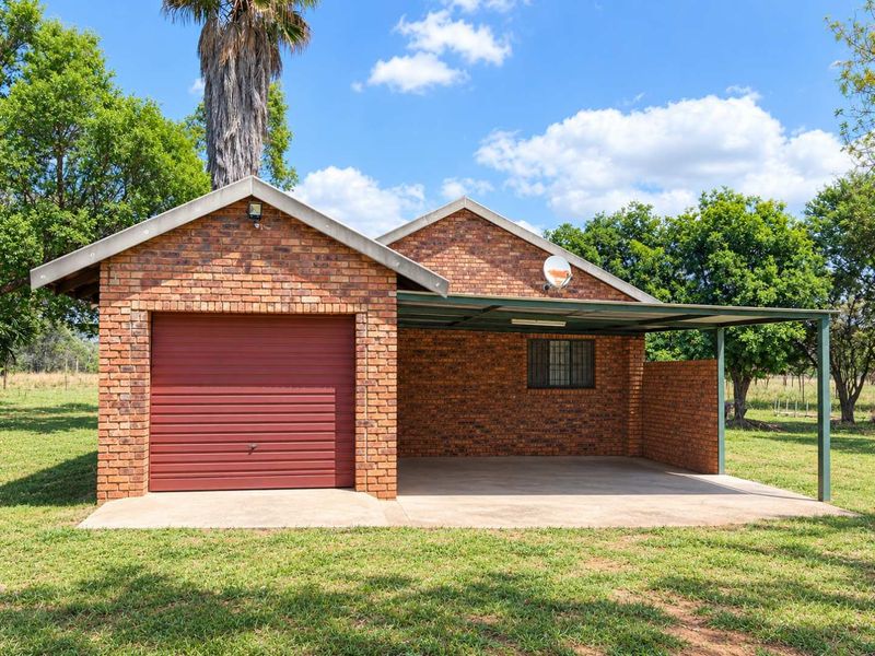 A well-maintained face brick garage featuring a secure roll-up door and an attached covered carport, situated on a spacious lawn.