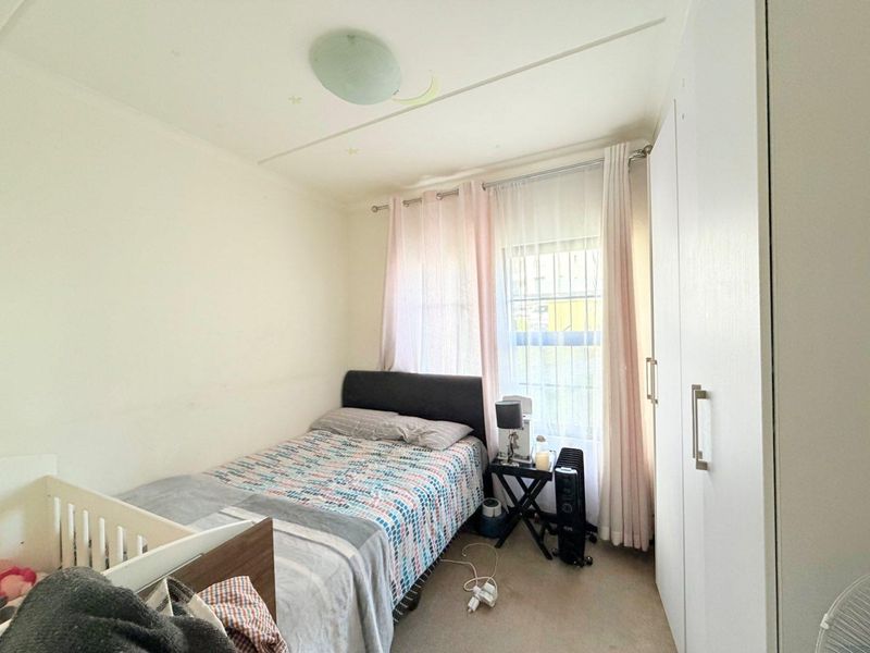 A compact bedroom featuring built-in cupboards and a window fitted with security bars, providing functional storage and natural light.