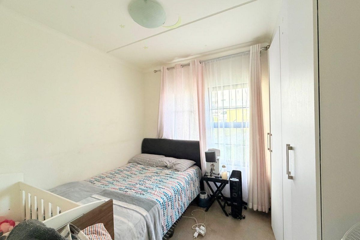 A compact bedroom featuring built-in cupboards and a window fitted with security bars, providing functional storage and natural light.