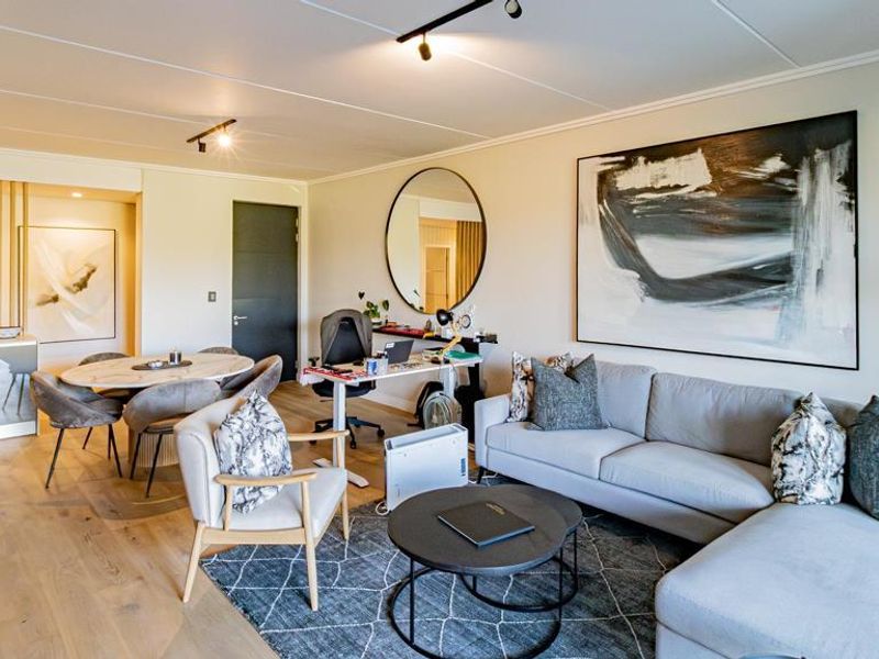 A bright open-plan living and dining area featuring light timber flooring, modern track lighting, and a decorative timber slat partition.