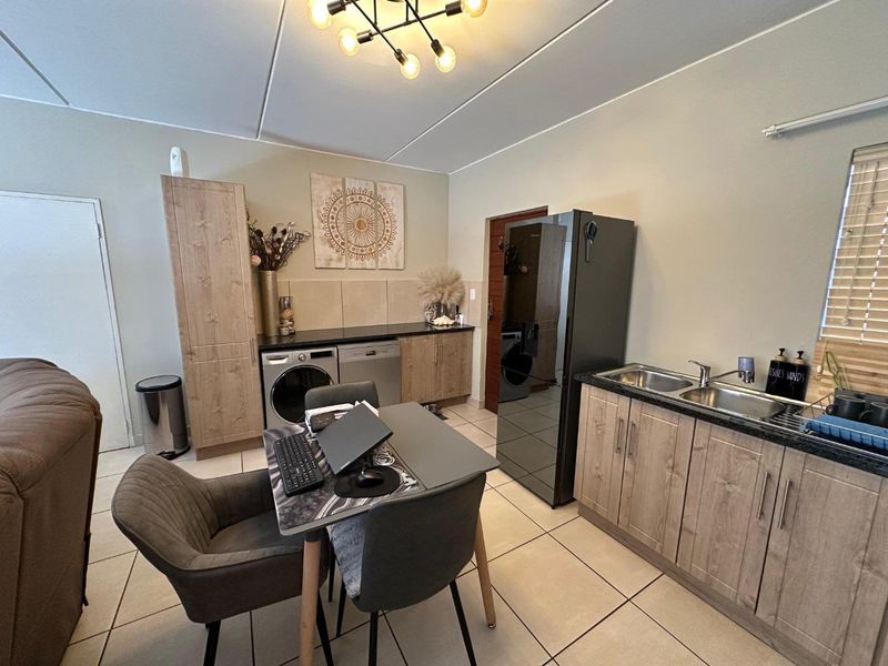 A functional kitchen area featuring wood-look cabinetry, double basin sink, tiled flooring, and integrated laundry plumbing connections.