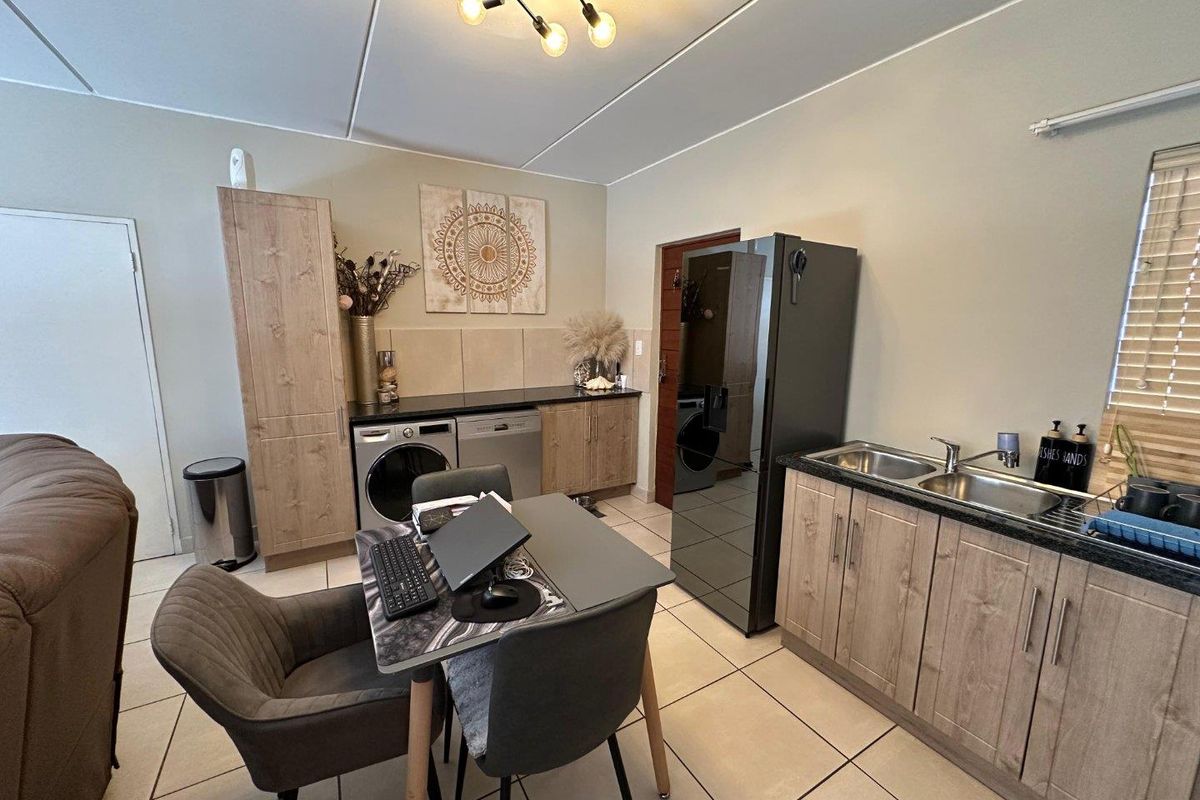 A functional kitchen area featuring wood-look cabinetry, double basin sink, tiled flooring, and integrated laundry plumbing connections.