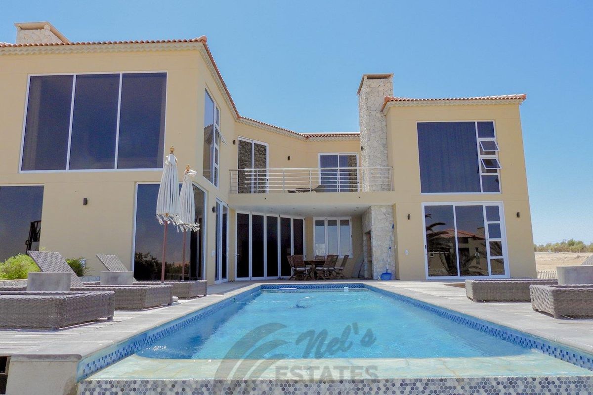 Rear view of a modern two-story house featuring a swimming pool, stone-clad chimney, balcony, and large glass sliding doors.