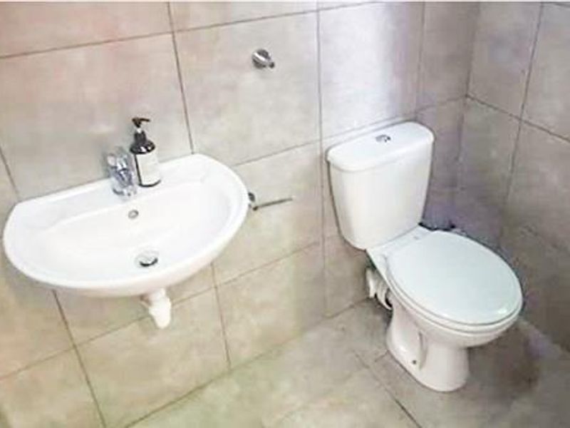 A compact bathroom featuring a wall-mounted basin and a standard toilet with neutral ceramic wall and floor tiling.