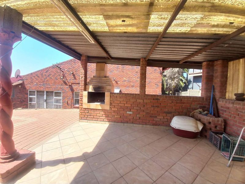 Covered outdoor patio featuring a built-in brick braai, tiled flooring, and exposed brick pillars, providing a functional space for outdoor entertaining.