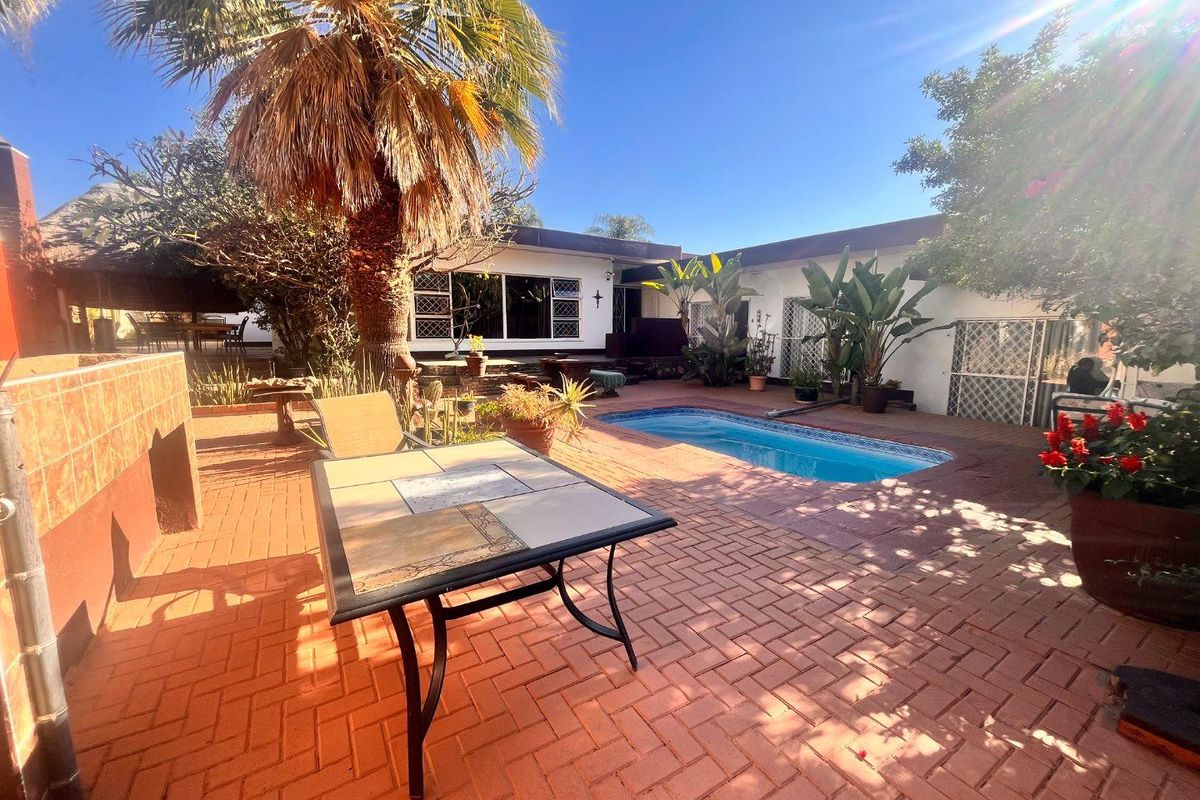 Outdoor entertainment area featuring a swimming pool, brick-paved patio, and a built-in braai, set within a private rear garden space.
