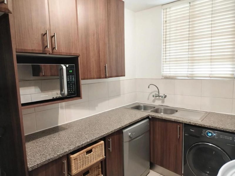 A functional kitchen featuring wood-look cabinetry, granite countertops, a double stainless steel sink, and a built-in microwave with tiled splashbacks.