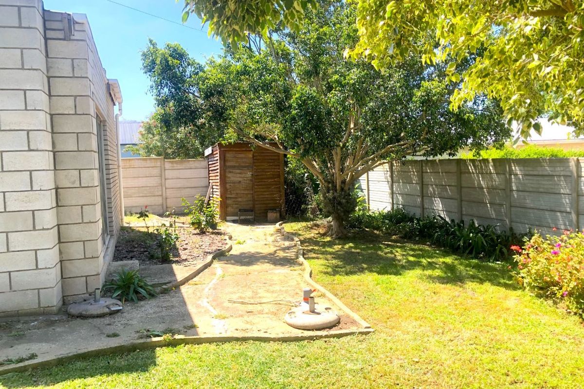 A private rear garden featuring a concrete pathway, established trees, and perimeter precast concrete walling, providing a functional outdoor space.