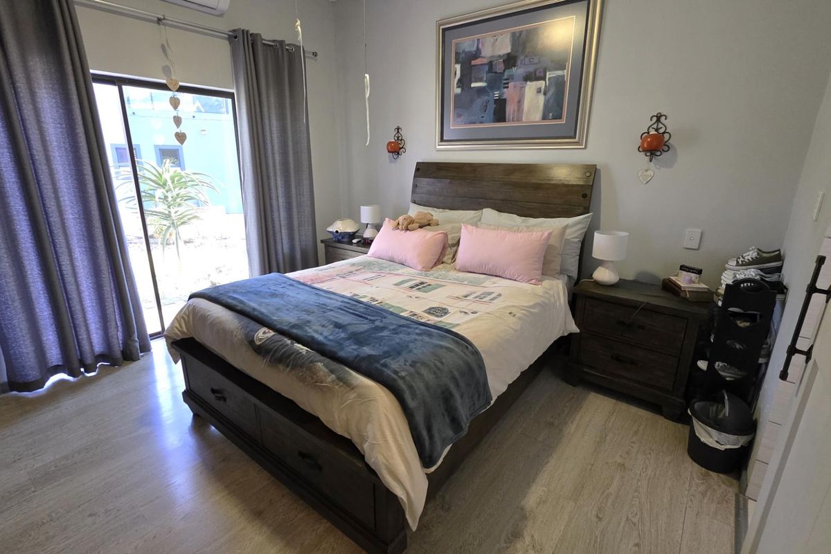 A well-maintained bedroom featuring light-toned laminate flooring, an air conditioning unit, and a sliding glass door providing direct access to the exterior.