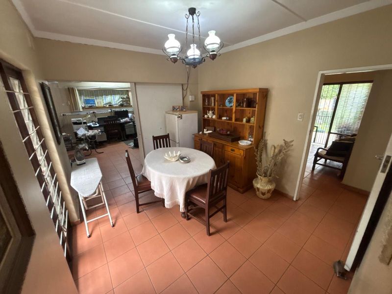 A dining area featuring tiled flooring and a central light fixture, providing access to adjacent rooms and an outdoor patio area.