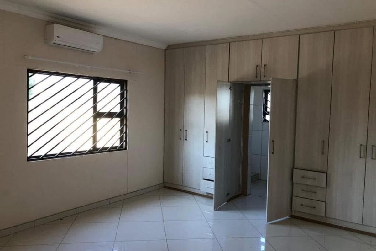Spacious bedroom featuring extensive built-in cupboards, tiled flooring, and a wall-mounted air conditioning unit.