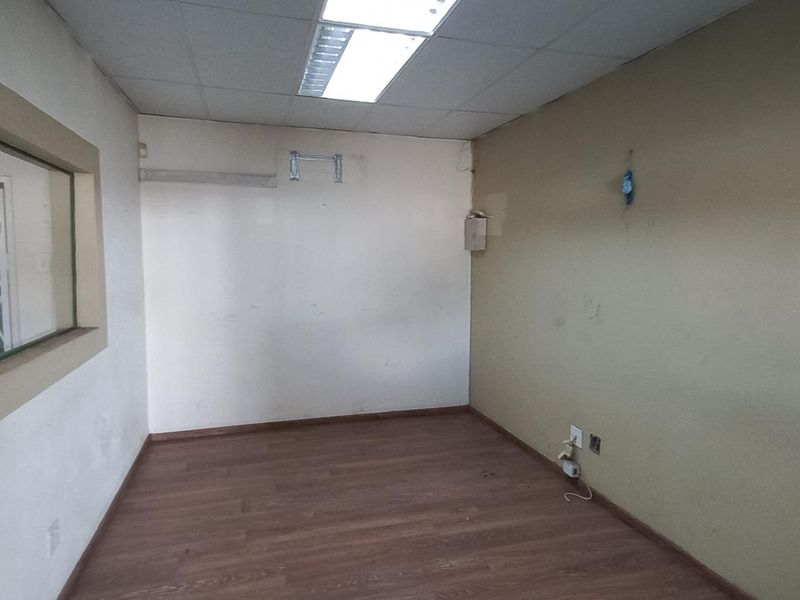 An empty office space featuring wood-look laminate flooring, a drop ceiling with recessed lighting, and an internal window with security bars.