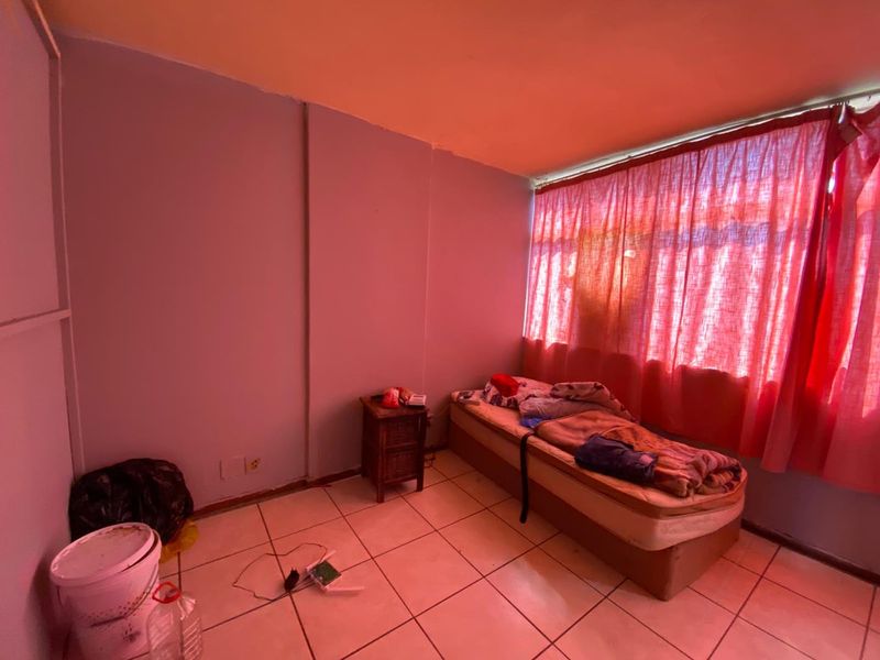 A bedroom featuring tiled flooring and a large window with red curtains, requiring cosmetic updates to improve the overall aesthetic and condition.
