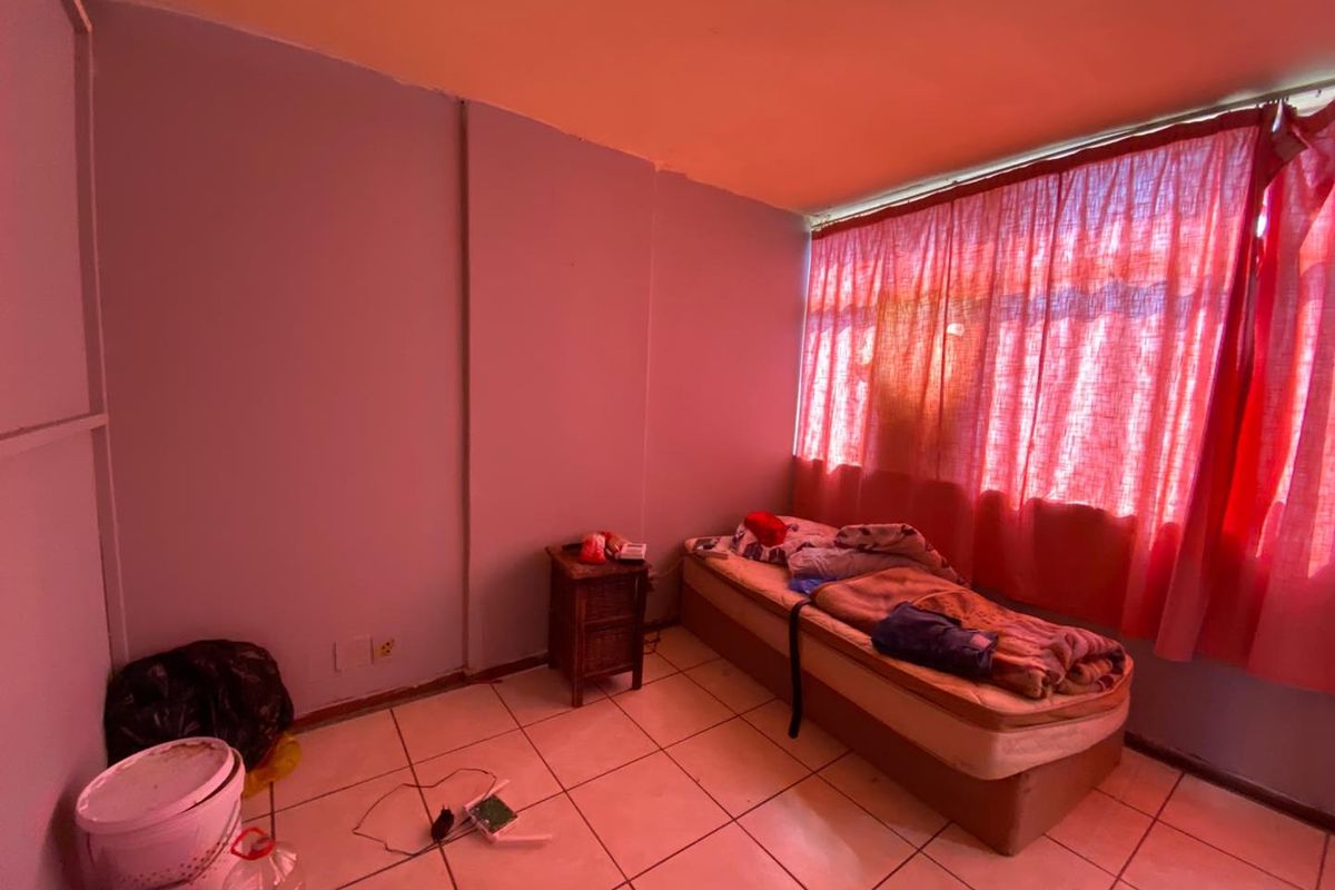 A bedroom featuring tiled flooring and a large window with red curtains, requiring cosmetic updates to improve the overall aesthetic and condition.