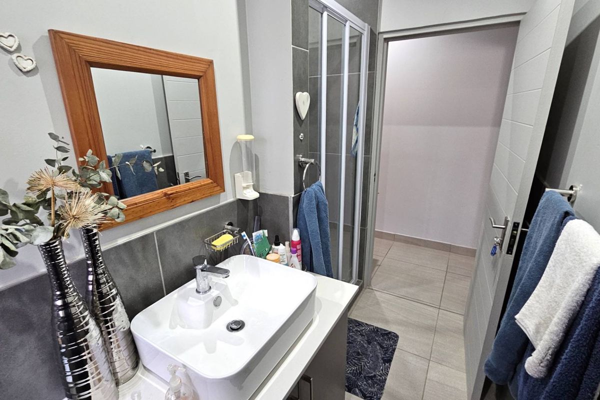 A modern bathroom featuring a vessel sink vanity, tiled splashback, and a glass-enclosed shower unit with neutral floor tiling.